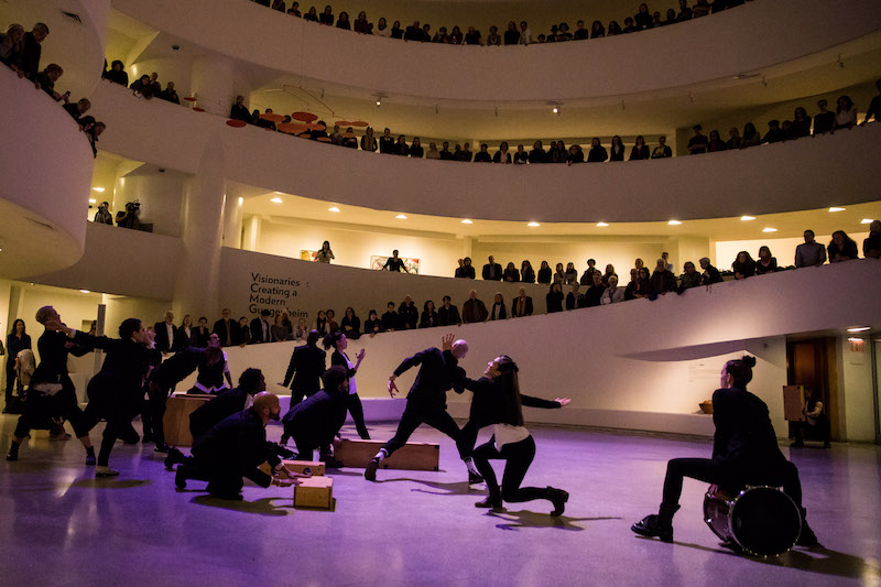 Michelle Dorrance sits on a bass drum while her ensemble tap and make rhythms with their bodies. No two performers execute the same move.